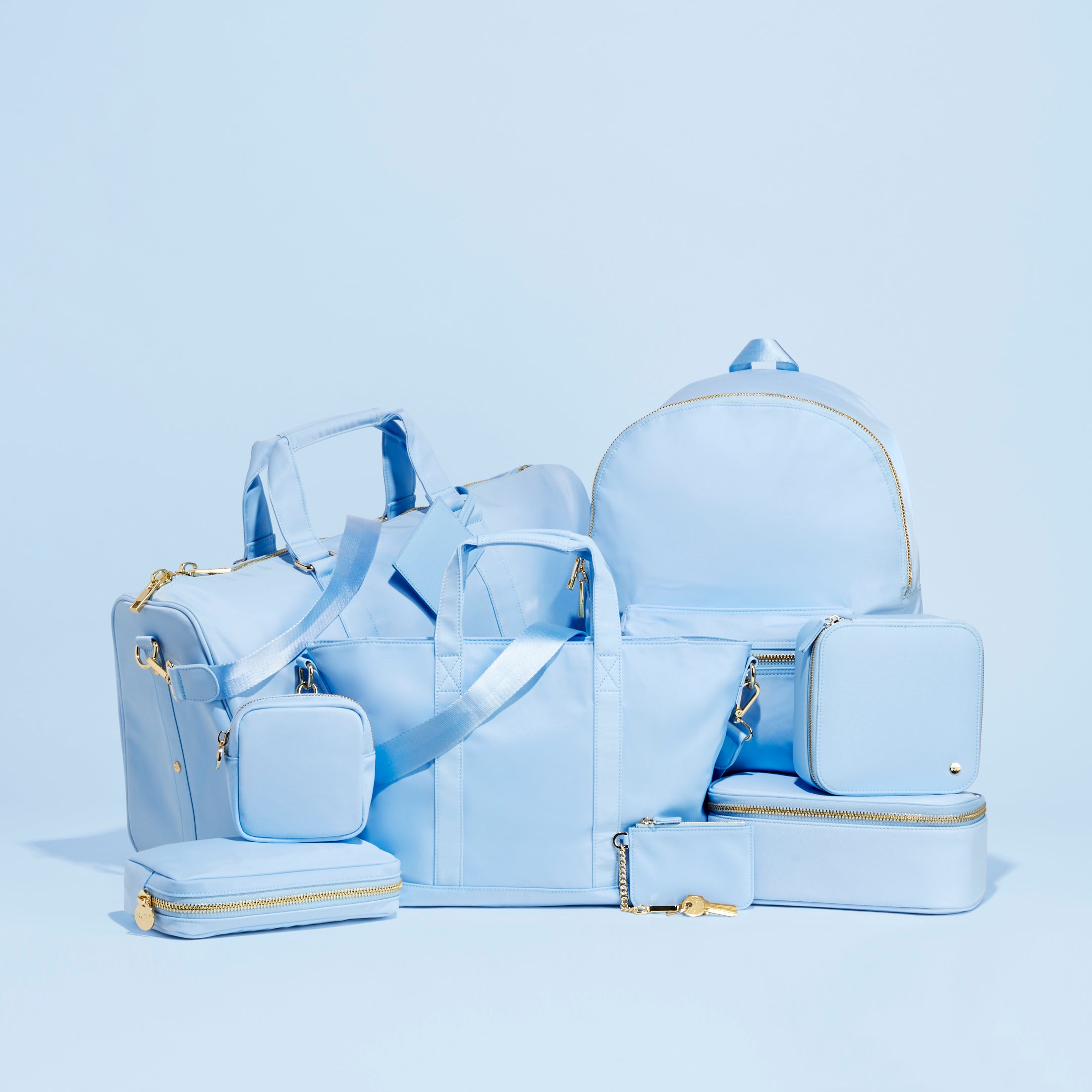 Set of light blue bags including a backpack, shoulder bag, and pouches on a light blue background