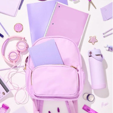 Pink backpack surrounded by stationery items on a white background